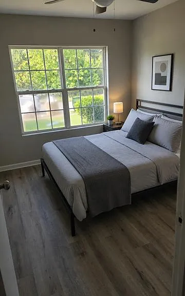 Comfortable bedroom featuring a full bed, nightstand lighting, and a large window overlooking the yard.