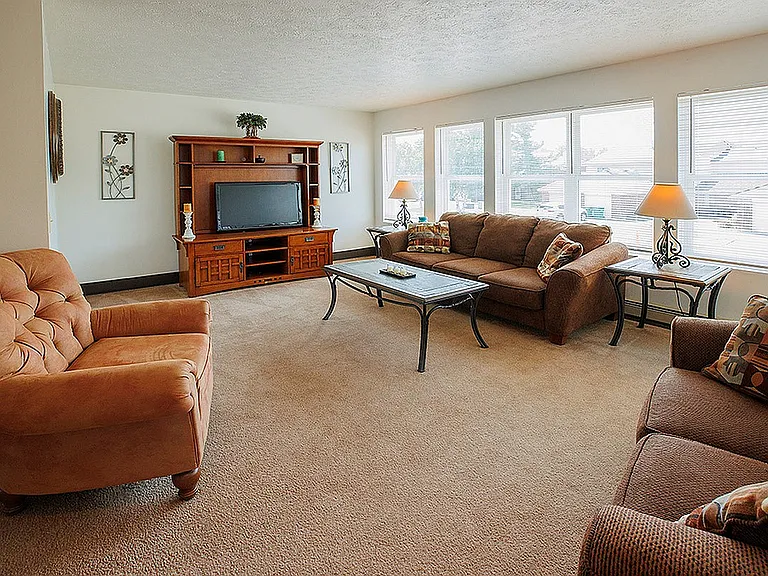 Cozy living room with plush brown sofas, large windows allowing natural light, and a stylish entertainment center.
