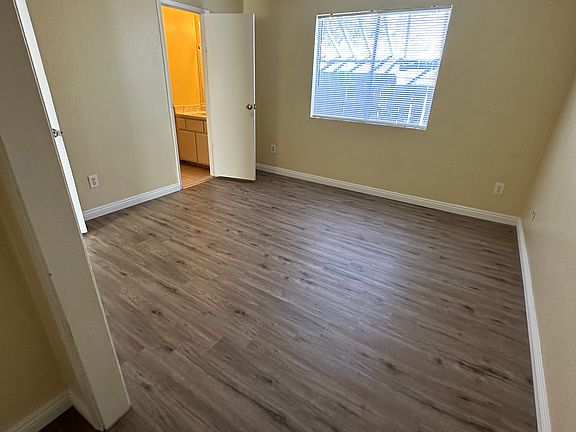 Light, sheer curtains drape gracefully over the windows, diffusing the sunlight and casting gentle shadows that dance across the polished hardwood floors.