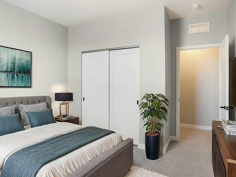 Elegantly designed bedroom featuring a plush gray upholstered bed, modern decor, and a stylish potted plant for a touch of nature.