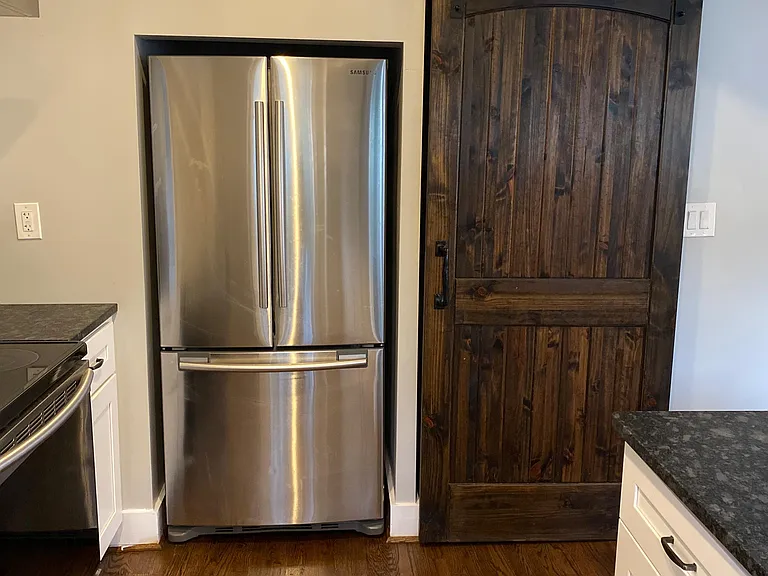 Kitchen area featuring a stainless-steel French-door refrigerator, ample cabinetry, and a sliding barn-door pantry.