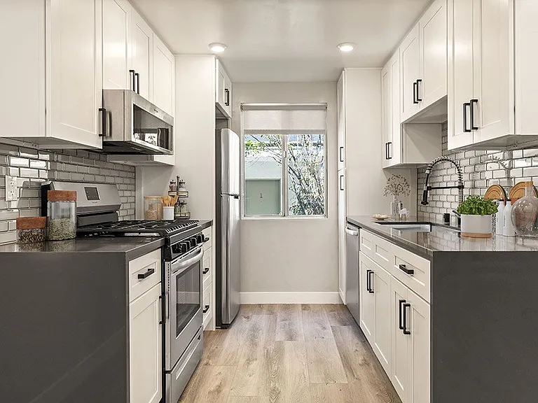 Tiled kitchen with stainless steel microwave, oven, fridge, and fixtures.