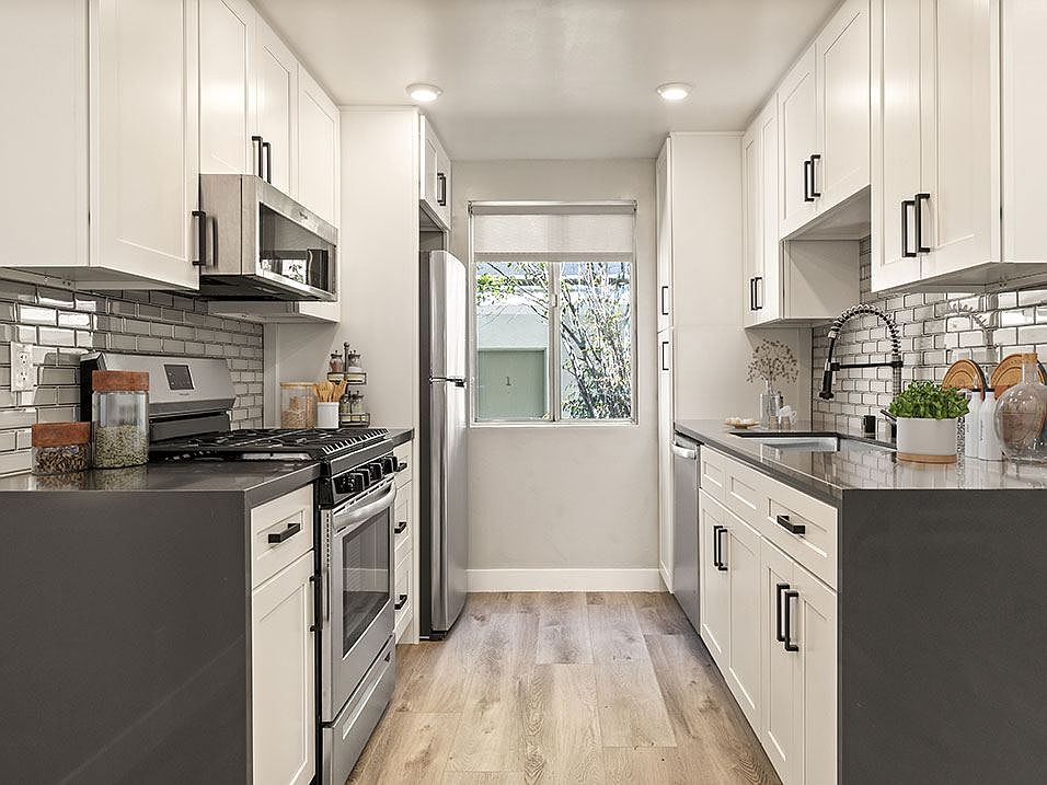 Tiled kitchen with stainless steel microwave, oven, fridge, and fixtures.