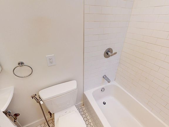 Bathroom with tub, tiled wall, hexagonal floor tiles, and small sink