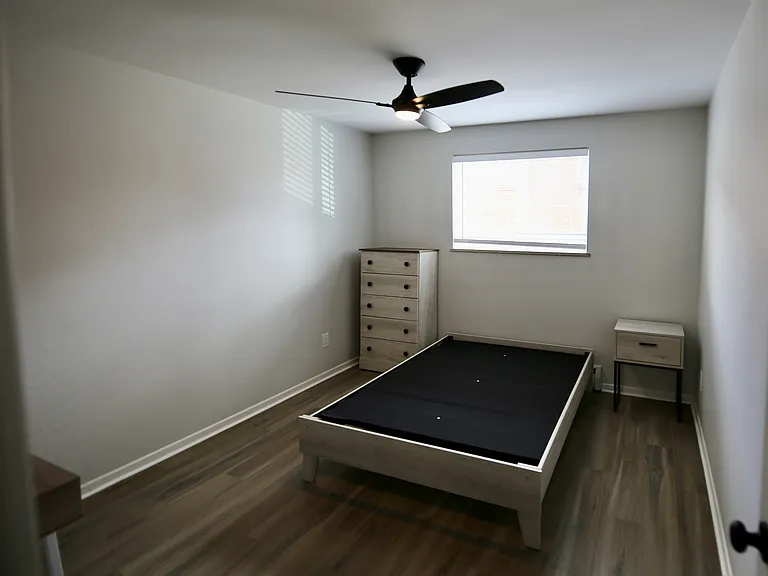 Inviting bedroom with modern ceiling fan, hardwood floors, and ample natural light, perfect for relaxation.
