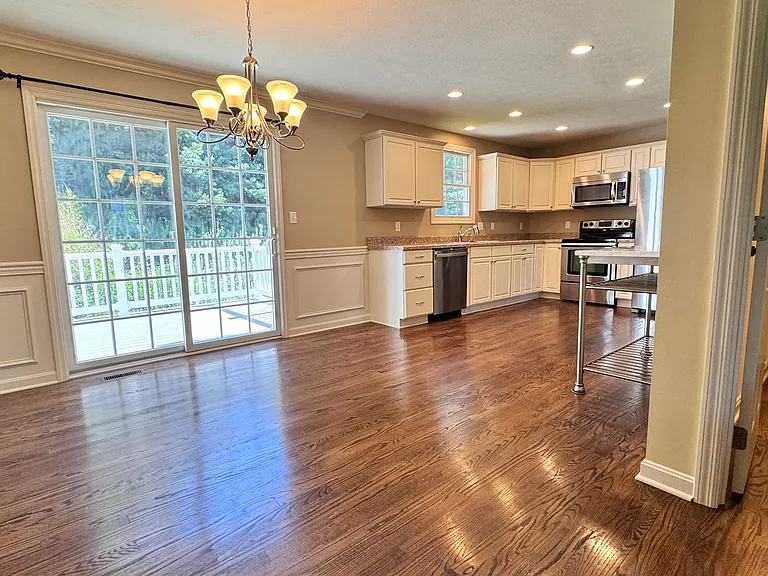 Spacious kitchen and dining room with walnut hardwood floors, bright cabinets, movable island, and access to large deck overlooking the backyard.