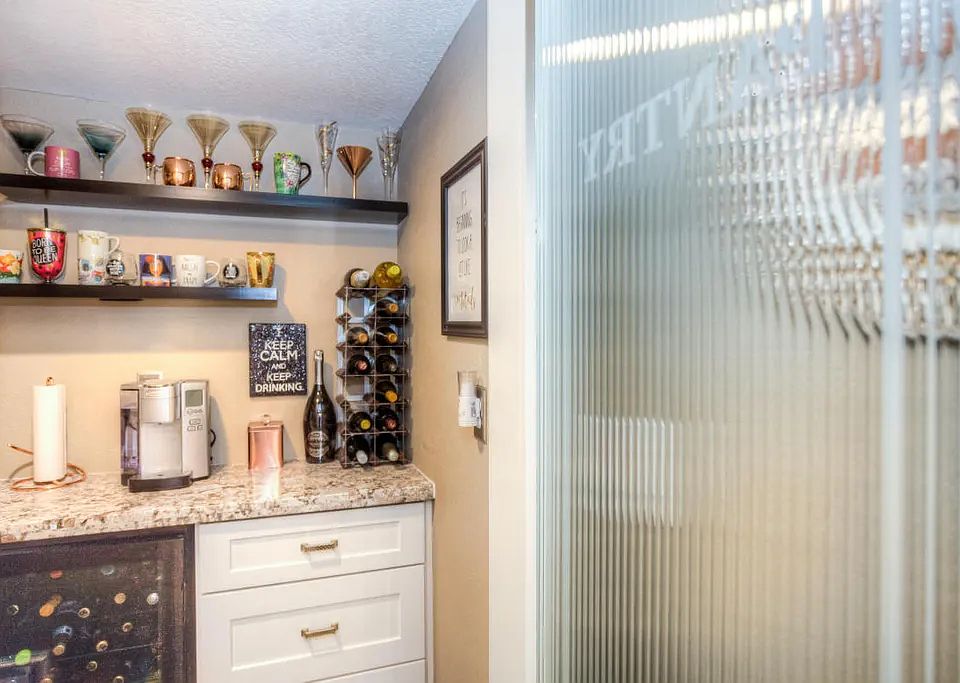 Pantry coffee or wine station area with wine fridge and floating shelves and granite counter.