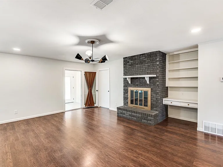 Living area featuring wood-finish flooring, a painted brick fireplace with a white mantel, recessed lighting, and a built-in shelving unit with a desk