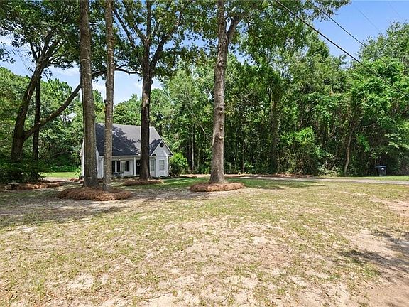 Single-story dwelling with white siding and a dark roof, framed by mature trees and natural landscaping