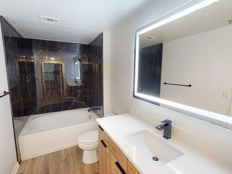 Apartment bathroom with large soaking tub, wood-style flooring and LED vanity mirror.