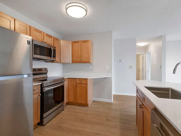 Renovated Package I kitchen with stainless steel appliances, white quartz countertops, maple cabinetry, white tile backsplash, and hard surface flooring