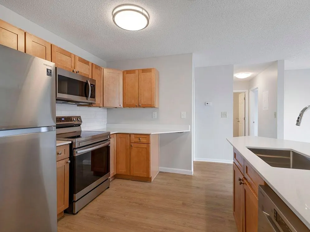Renovated Package I kitchen with stainless steel appliances, white quartz countertops, maple cabinetry, white tile backsplash, and hard surface flooring - Avalon Burlington