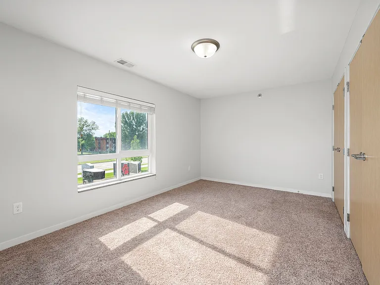 Bright and spacious bedroom with plush carpet, large window offering a scenic outdoor view, and modern closet doors. Bright and spacious bedroom with plush carpet, large window offering a scenic outdoor view, and modern closet doors.