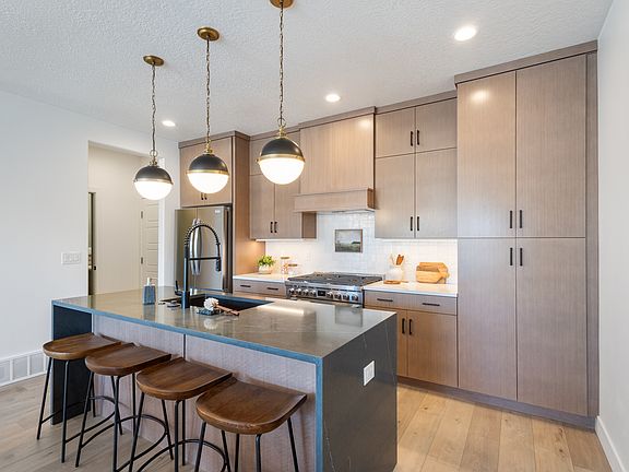 Modern kitchen with wood cabinets, an island with a dark countertop and sink, four wooden stools, ha