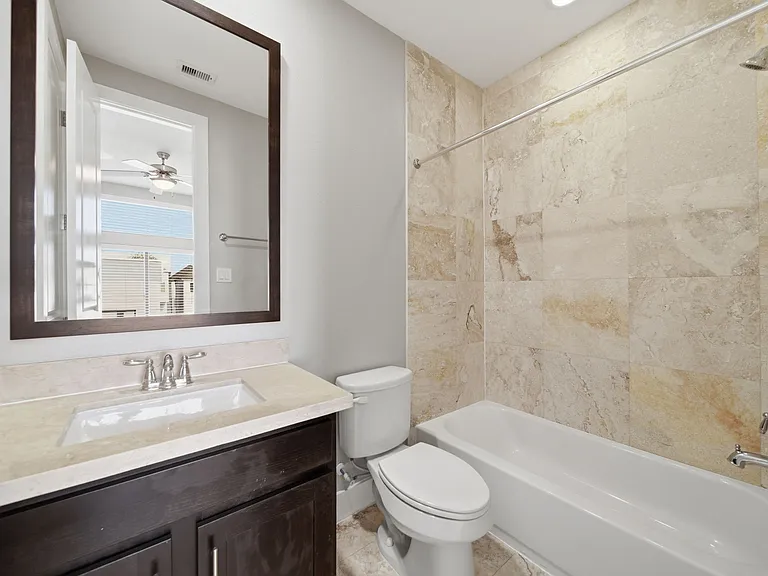 Third-floor ensuite bedroom features a sleek, modern bathroom with a stylish vanity, large mirror, and tub with full tile surround. Natural light enhances the neutral finishes, creating a bright and inviting spa-like feel.