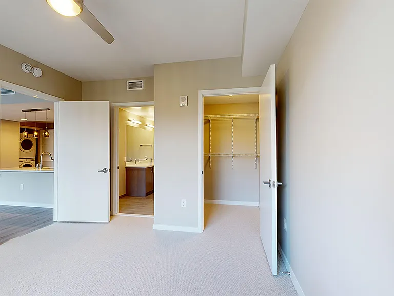 Spacious apartment bedroom with large closet, attached bathroom and plush carpet flooring.