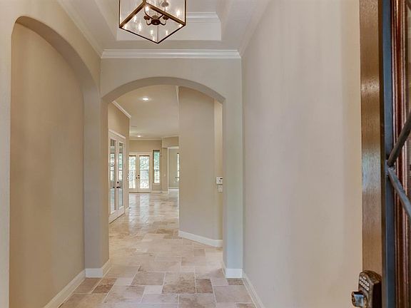 From the foyer notice the beautiful Travertine tile that flows through the home. Secondary bedroom to the left. Side patio opens through the french doors to the left. The living area and separate dining room open at the back.