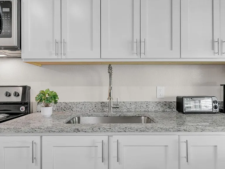 Kitchen features ample shaker-style cabinetry, granite-look counters, and a centered sink with gooseneck faucet for easy prep