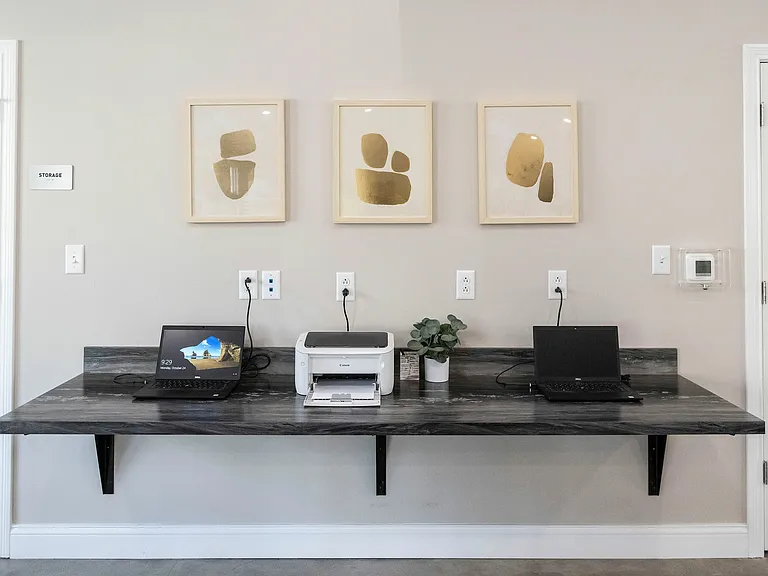 Modern home office setup with sleek black countertop, two laptops, a printer, and minimalistic wall art for a contemporary workspace.