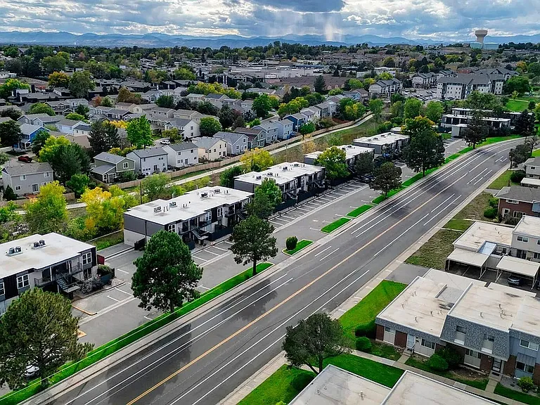 Aerial view of a charming residential neighborhood with tree-lined streets and modern townhouses, offering a picturesque suburban lifestyle with mountain views in the distance.