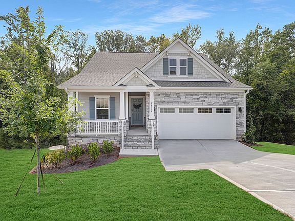 A house with a white garage door and a porch surrounded by trees.