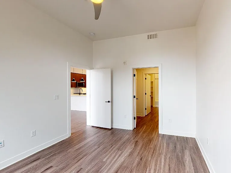Spacious apartment bedroom with large closet, attached bathroom and wood-style flooring.
