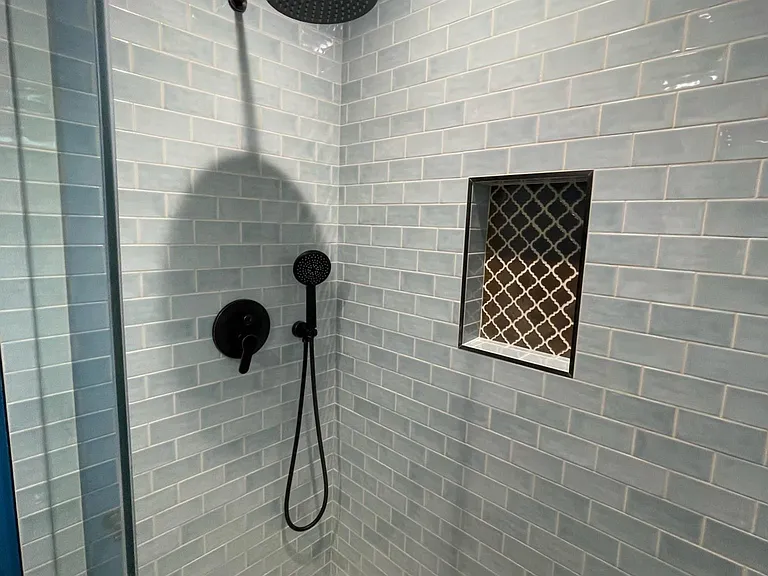 Beautiful rainfall shower head with handheld sprayer and wall enclave for toiletries.