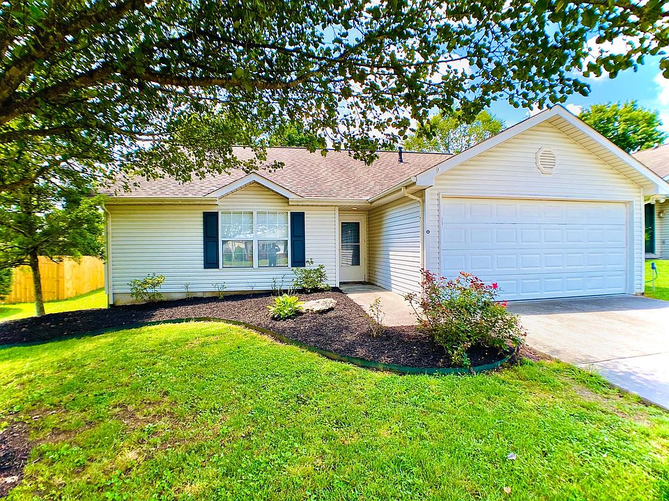 Front view of house- has a large shade tree & a garden area.