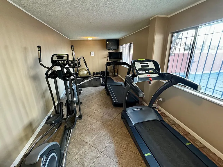 24-hour fitness room with treadmills, bike, elliptical, dumbbells, and pool view.