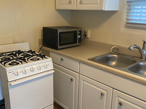 Kitchen area includes oven, refrigerator, shelves for storage, and sink.