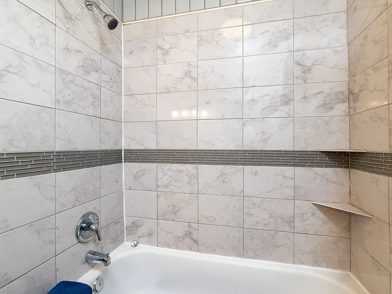 Bright, clean bathroom featuring a modern vanity with black fixtures and a fully tiled tub/shower combo. Marble-style walls, a bold blue curtain, and sleek accents create a fresh, polished space for getting ready or unwinding.