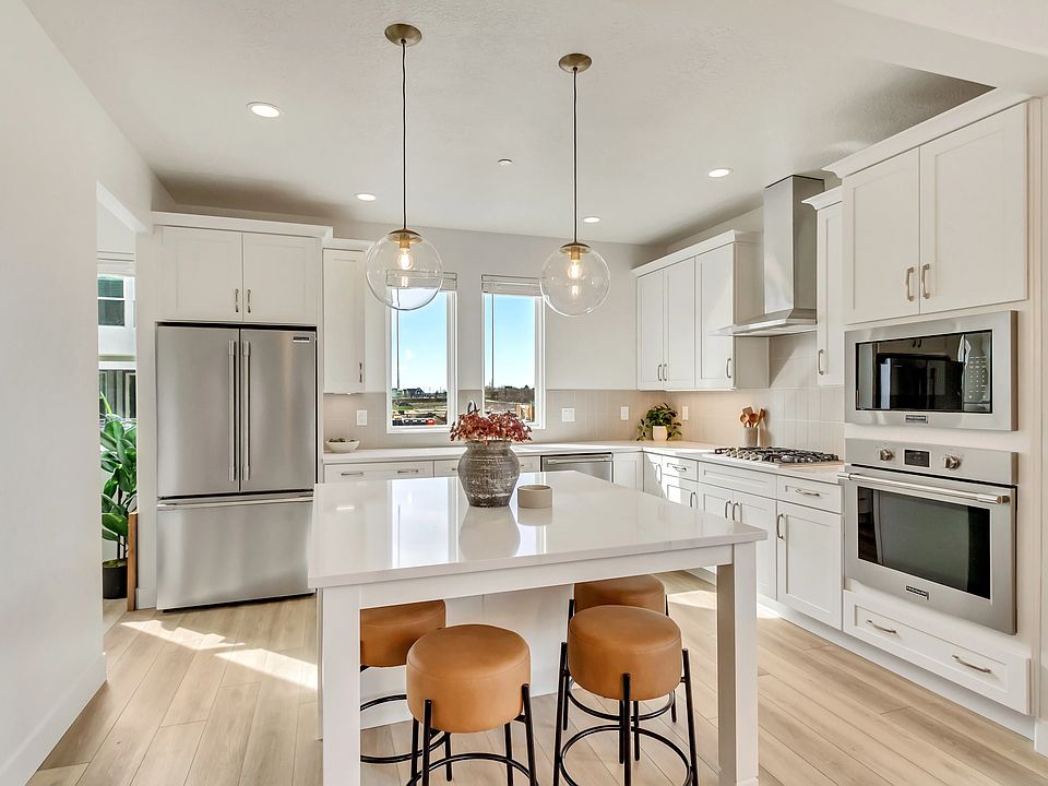 A modern kitchen with white cabinets and a large central island featuring three brown stools. The st