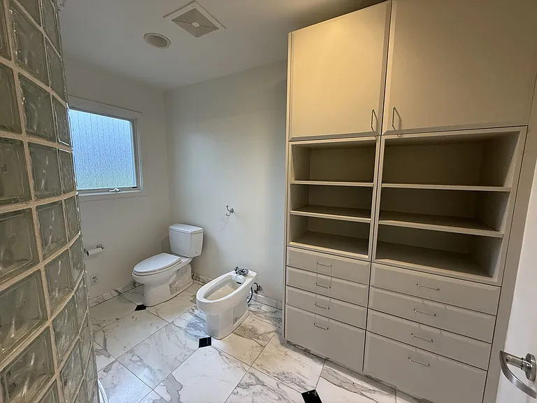 In-suite primary bathroom is tastefully appointed with glass block walls featuring dual sinks, Jacuzzi tub, multi-jet shower stall, a bidet, and a walk-in closet with built-in organized storage.