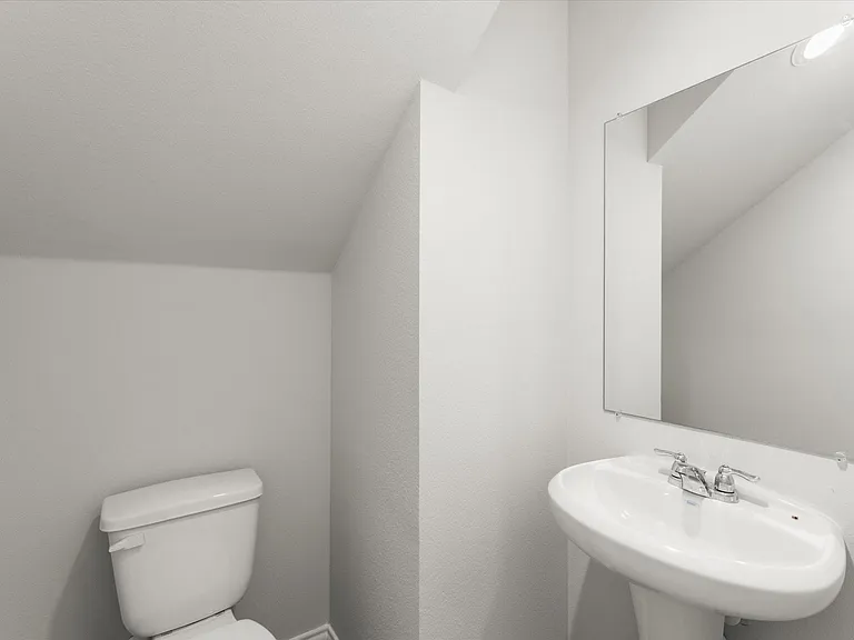 Bright white powder room featuring a pedestal sink with chrome faucet, a rectangular wall-mounted mirror, and a commode
