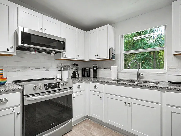 U-shaped kitchen with ample shaker cabinetry, stainless range, low-profile microwave, & double sink set under a large window.
