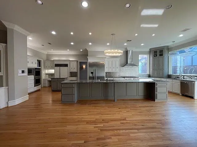 Kitchen featuring gray cabinets, ornamental molding, a breakfast bar area, built in appliances, and hanging light fixtures