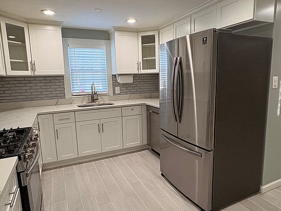 Beautiful kitchen with tile floor, white cabinetry, french door refrigerator, gas stove, dishwasher, microwave. Sink window overlooks the backyard.