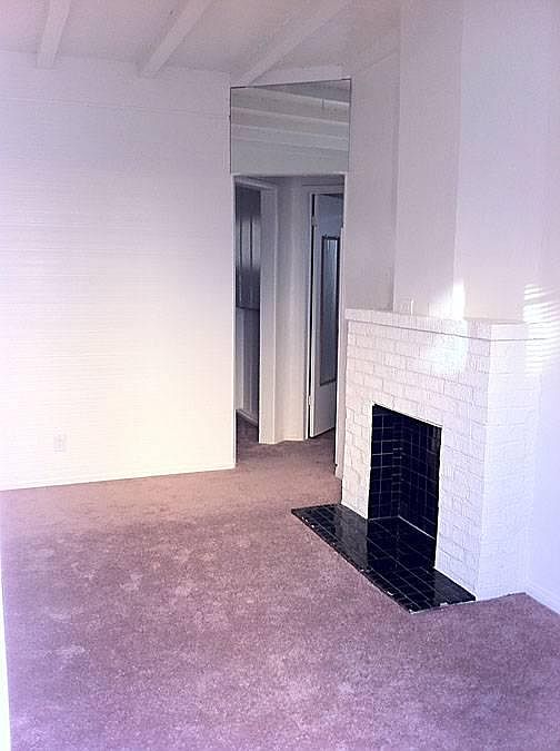 Living room with faux fireplace and view to bedroom and bath