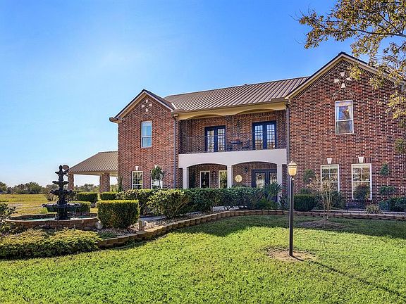 The front of this beautiful custom home features landscaping with a fountain and a large upstairs balcony.