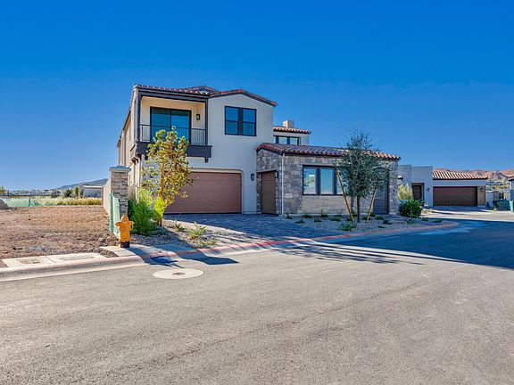 A modern, two-story residential house with a tile roof, surrounded by a paved driveway and landscape