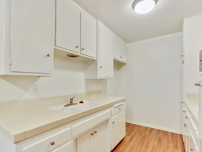 Kitchen with White kitchen cabinets and cupboards, Double white kitchen sink and Tile countertops on the right side, White Oven on the left side