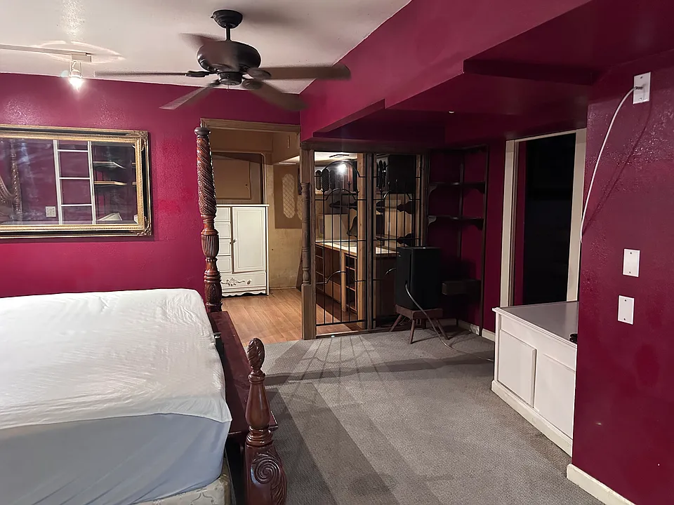 Master bedroom view showing King size bed and 4 poster frame with long view of office space and closet area behind.Pocket door to Master bathroom on right side.