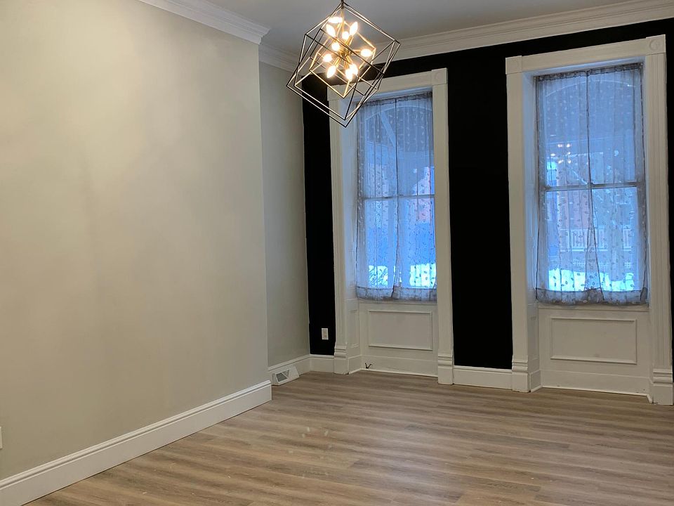 A shot of the living room, with modern chandler, recessed lighting, tall baseboards, laminate flooring and crown molding.