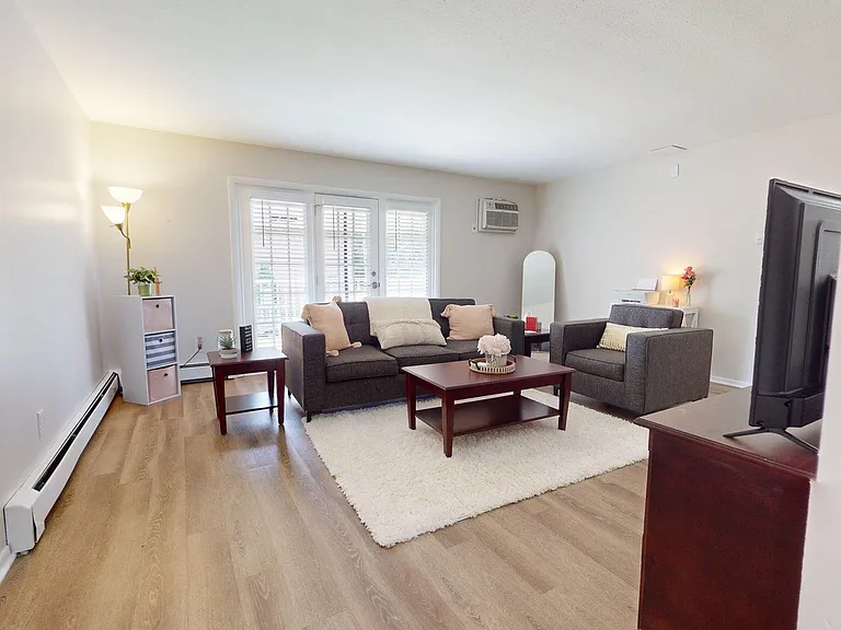 Bright and inviting living room with modern gray sofas, cozy white rug, and sleek wooden tables, enhanced by natural light from large windows. Bright and inviting living room with modern gray sofas, cozy white rug, and sleek wooden tables, enhanced by nat