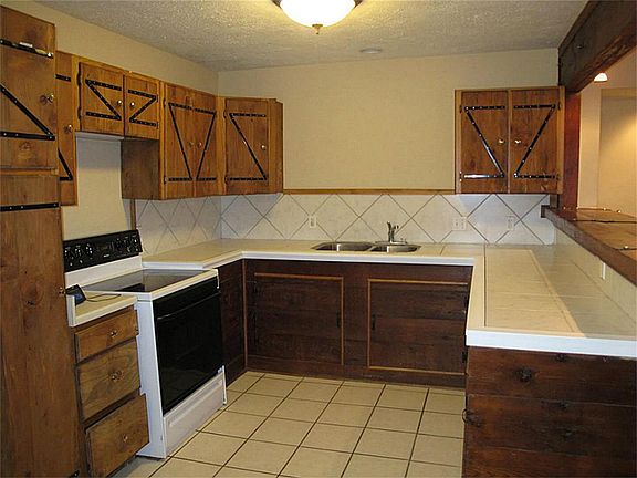 WONDERFUL kitchen features ceramic tile flooring, countertops, & backsplash, updated sink, light fixture, & cabinetry, and smoothtop range/oven combo.