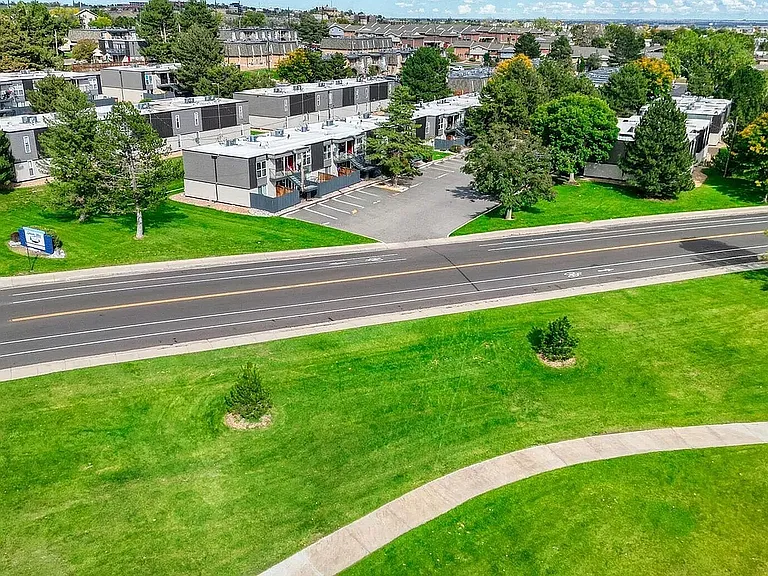 Aerial view of a charming apartment complex nestled among lush greenery, with a scenic road and vibrant community setting.