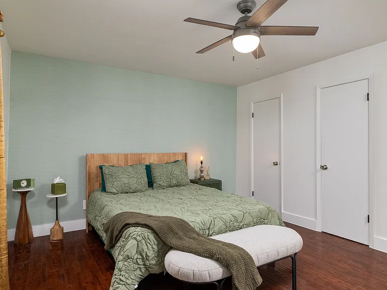 Rest in a calming bedroom with soft green tones, warm lighting, and a cozy bench at the foot of the bed. Enjoy a large TV, stylish dresser, and easy access to a spacious walk-in closet for a relaxing, comfortable stay.