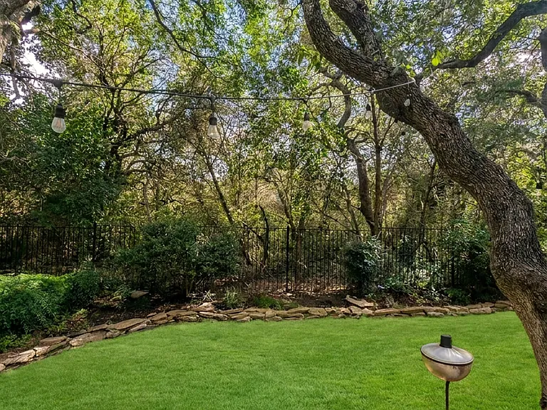 Greenbelt-backed yard framed by mature oaks and cafe lights