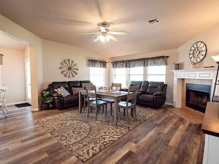 Open-concept living and dining area with large windows, ceiling fan, and fireplace, plus space for a full dining set.