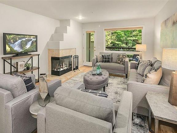 Spacious living room with a wood-burning fireplace and connected to a covered patio overlooking wooded area.